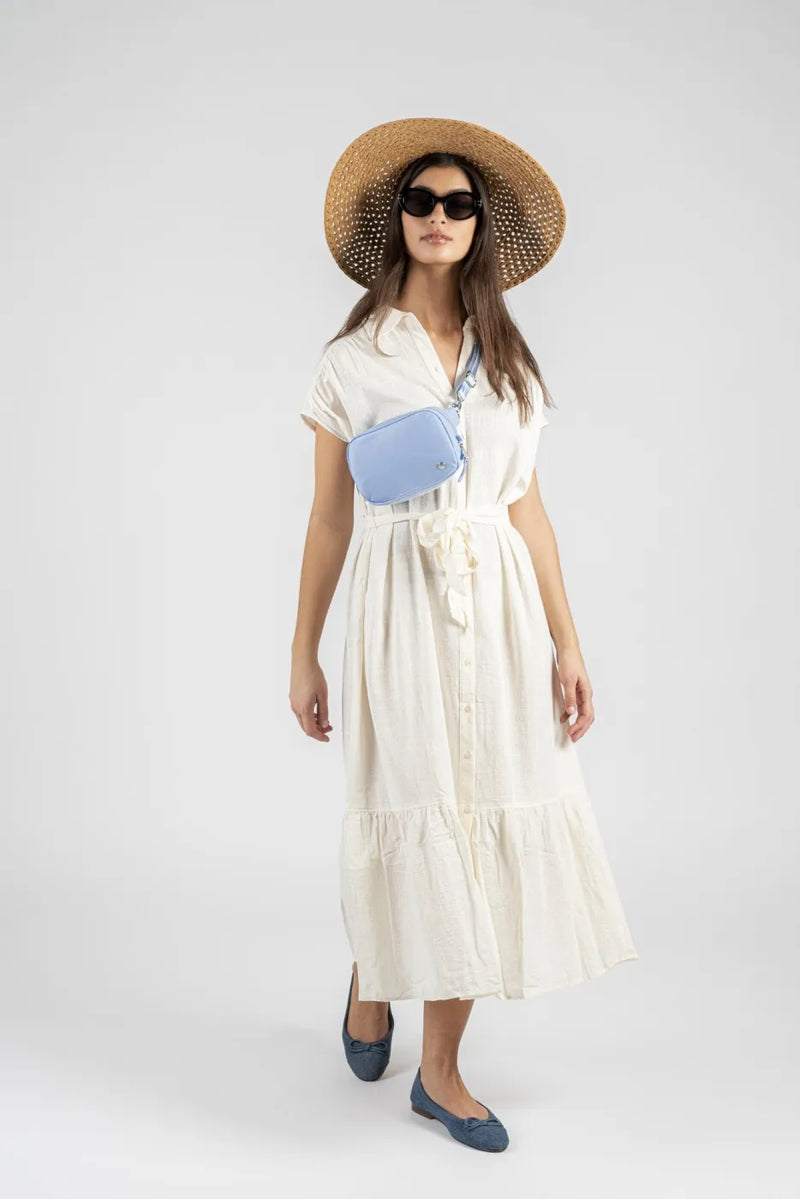 Pacsafe W Anti-theft Micro Sling in Serenity Blue, worn at the waist by a woman walking in a cream dress and straw hat