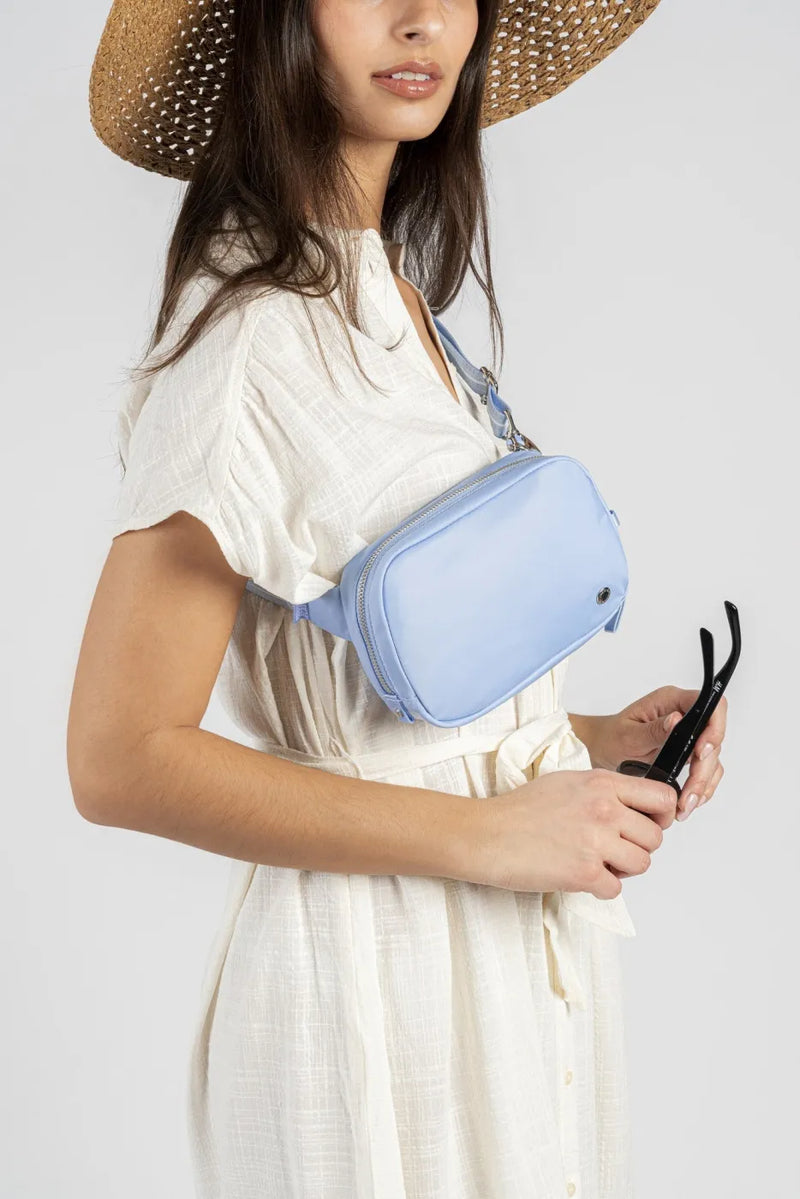 Pacsafe W Anti-theft Micro Sling in Serenity Blue, worn at the hip while sunglasses are taken from the front pocket
