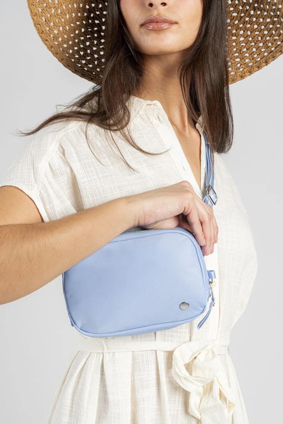 Pacsafe W Anti-theft Micro Sling in Serenity Blue, worn at the hip of a woman in a cream dress, hand resting on the bag