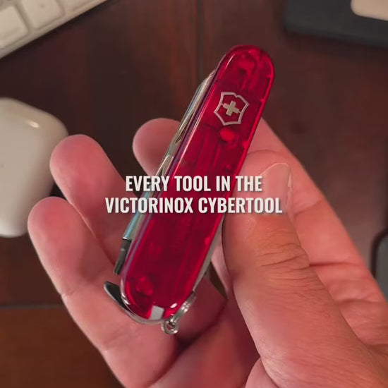 Victorinox CyberTool in translucent red on a wooden desk, opening the hex drive with its bit case, large and small blades, bottle opener and the pressurised ballpoint pen