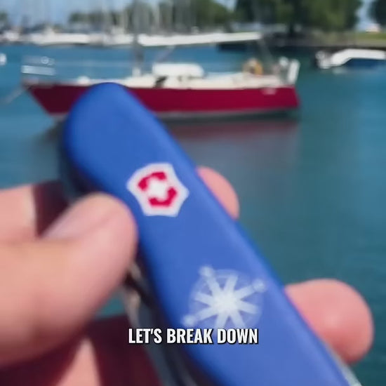 Victorinox Skipper Swiss Army Knife in blue held at a marina, showing the serrated blade, the shackle opener and marlin spike combo and the high-visibility red lanyard