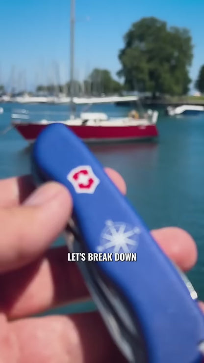 Victorinox Skipper Swiss Army Knife in blue held at a marina, showing the serrated blade, the shackle opener and marlin spike combo and the high-visibility red lanyard