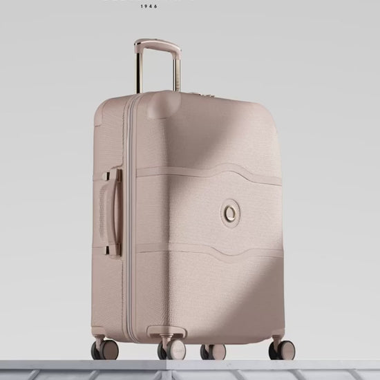 Delsey Chatelet Air 2.0 80th anniversary suitcase in beige rose: dual-density wheels, the gold double-layer zip teeth and lock, the blue deluxe lining, then the case on a stone plinth