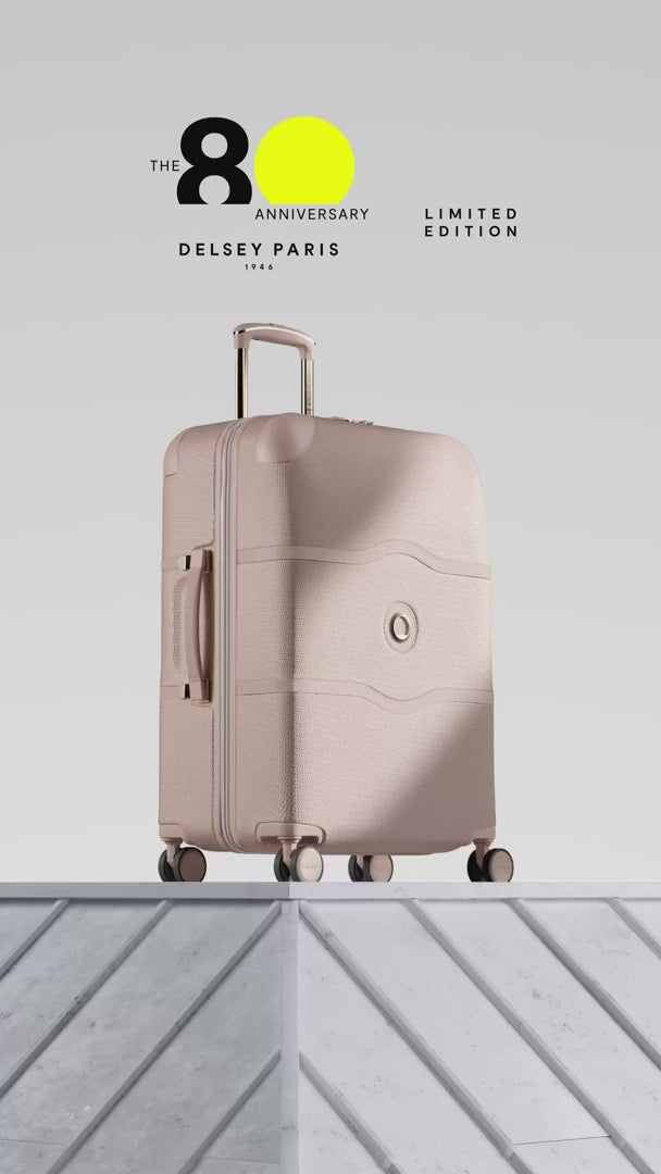 Delsey Chatelet Air 2.0 80th anniversary suitcase in beige rose: dual-density wheels, the gold double-layer zip teeth and lock, the blue deluxe lining, then the case on a stone plinth