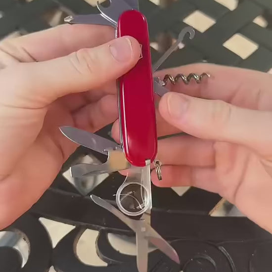 Victorinox Swiss Army Knife in red, its multipurpose hook untying a knot in a cord, propping up a phone, pulling an oven rack and lifting a ring-pull can lid