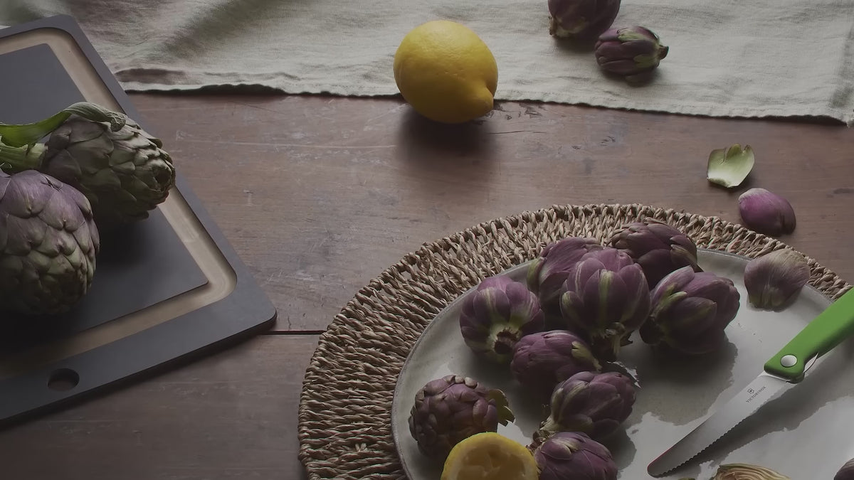 Victorinox Swiss Classic foldable paring knife in red unfolding beside artichokes and a lemon, then red, green and black knives laid on moss with sliced apples