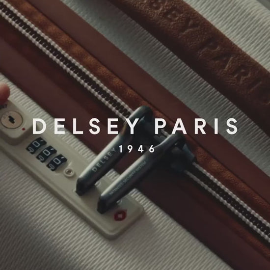 Delsey Paris film: a woman in a leather jacket in the city with a Chatelet Air 2.0 cabin case in angora white standing at the foot of an ornate stone doorway