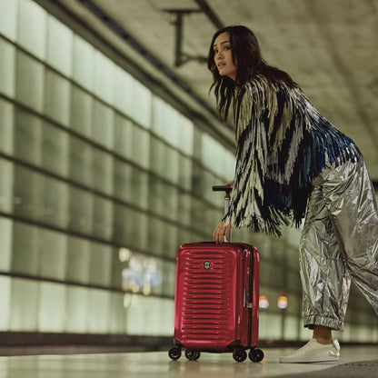 Victorinox Airox carry-on in red, silver and black: a traveller wheeling it through a station, the case opening butterfly-style to show packed clothes, and a man with it on an escalator