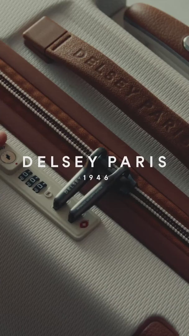 Delsey Paris film: a woman in a leather jacket in the city with a Chatelet Air 2.0 cabin case in angora white standing at the foot of an ornate stone doorway
