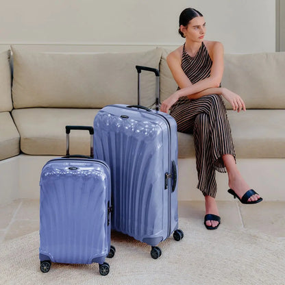 Woman sitting on a couch with two C-Lite Lavender suitcases in front of her.