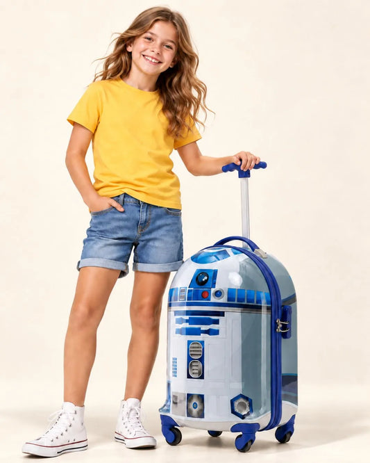 A young girl with long wavy brown hair stands next to a R2-D2 STAR WARS themed rolling carry on suitcase. She is wearing a yellow t-shirt, denim shorts, and white high-top sneakers.
