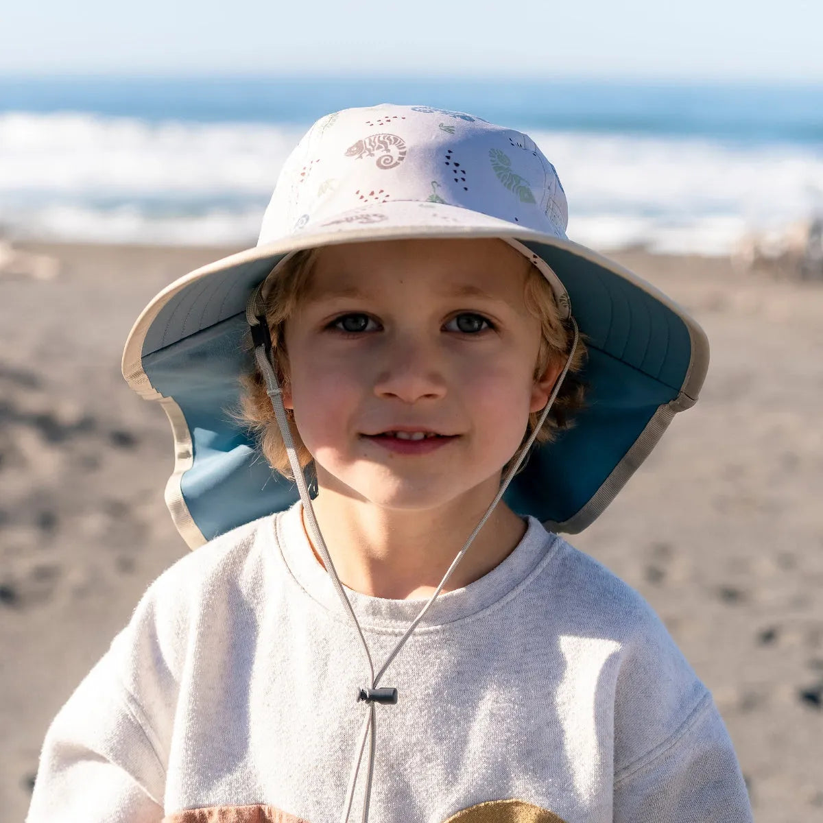 A young child wearing a Sunday Afternoons Kids Play Hat in dune grass