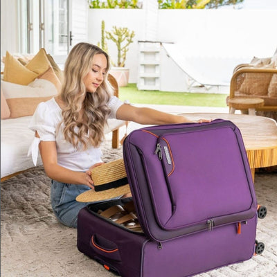 Woman packing a purple suitcase with a hat in a bright living room.