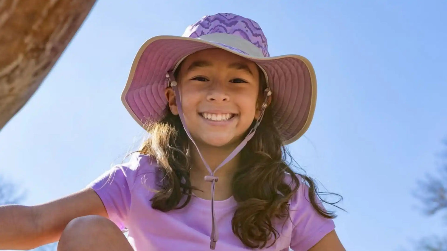 A smiling young girl in a purple sun hat.